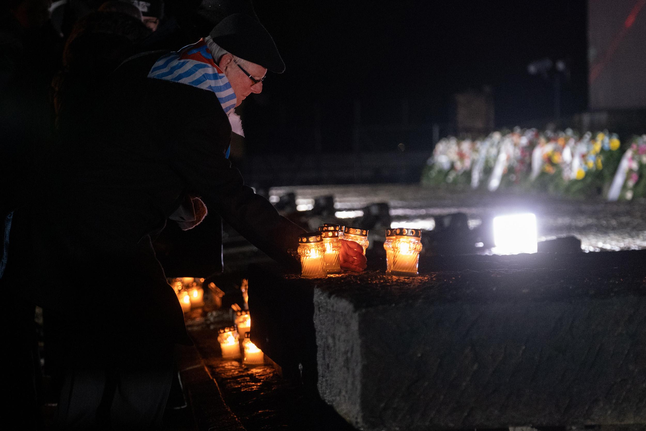 Přeživší holokaustu pokládá svíčku k památníku v nacistickém táboře smrti Birkenau během pietního aktu v polské Osvětimi, 27. 1. 2024. (FOTO: Auschwitz-Birkenau State Museum, Wojciech Grabowski)